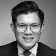 A trusted financial professional, wearing glasses and a suit, smiles at the camera in a black and white portrait.